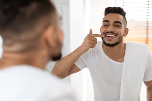 man looking at teeth in the mirror