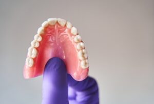 Fingers,In,Purple,Gloves,Holding,Set,Of,Dentures.,Dental,Plan